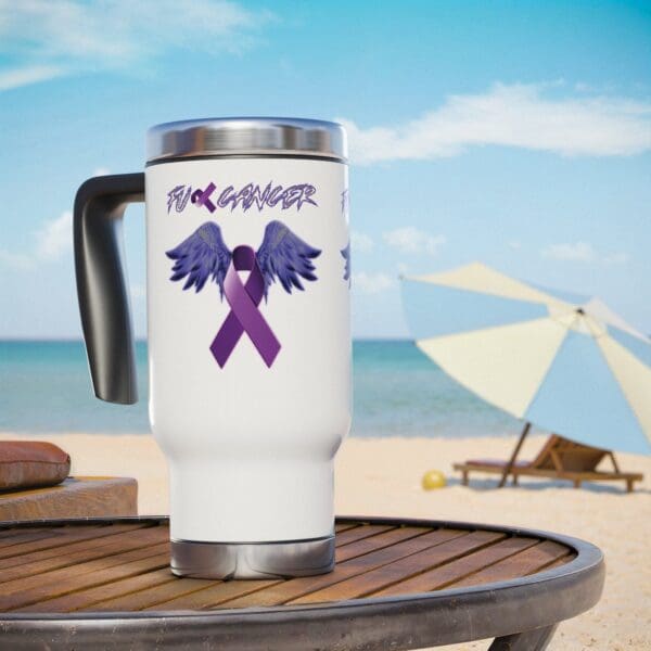 F*ck Cancer Stainless Steel Travel Mug with Handle, 14oz, featuring a purple ribbon and wings design alongside an anti-cancer message, placed on a beach table with an umbrella and lounge chair in the background.