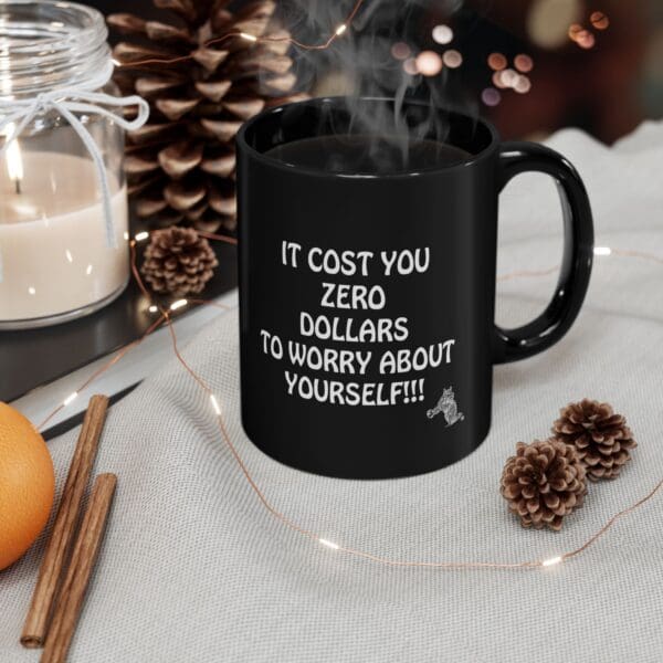 The "Zero Dollars Coffee Mug" featuring the text "It cost you zero dollars to worry about yourself!!!" is placed on a gray cloth near a candle, pinecones, an orange, and cinnamon sticks.