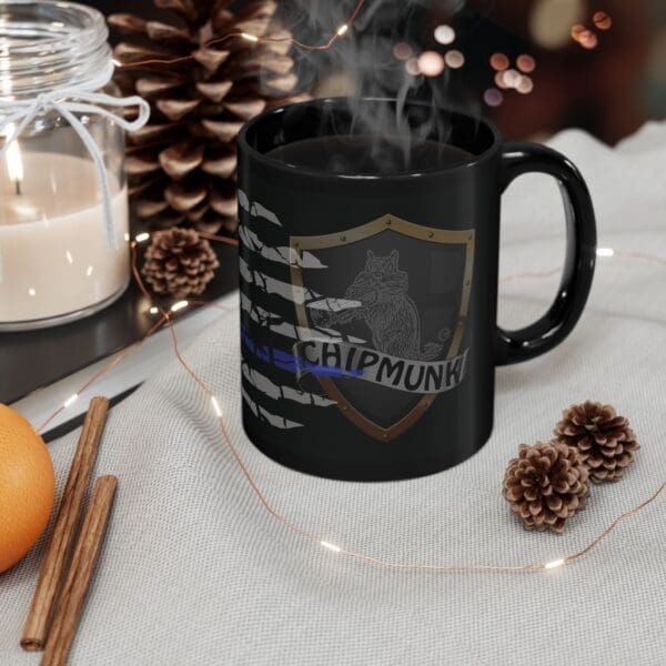 The Police Support Coffee Mug with a wolf emblem and "Chipmunk" text is filled with a steaming hot beverage. The mug is placed on a table adorned with pinecones, a candle, cinnamon sticks, and festive decor around it.