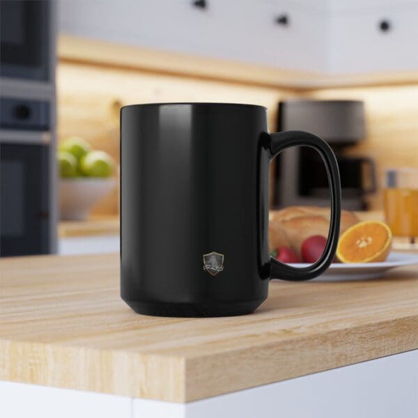 A black Angry Cat Coffee Mug rests on a wooden kitchen counter with a plate of fruit in the background.