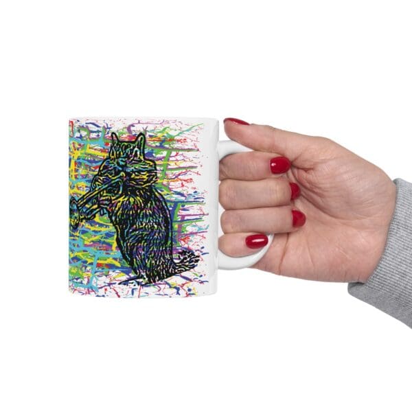 Hand holding a Cracked Chipmunk Coffee Mug, featuring a colorful, abstract painting of a raccoon against a vibrant background.