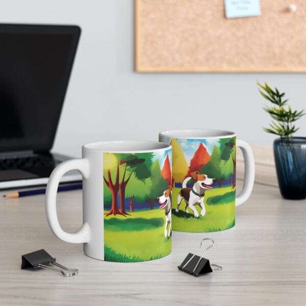 Two Playful Dog Coffee Mugs 11oz, featuring a dog in a colorful park scene, are on a desk with a laptop, plant, and binder clips.