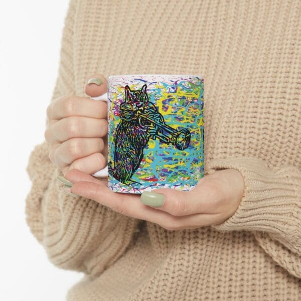 Person in a beige sweater holding a Cracked Chipmunk Coffee Mug adorned with a colorful, abstract image of a cat playing the trumpet.