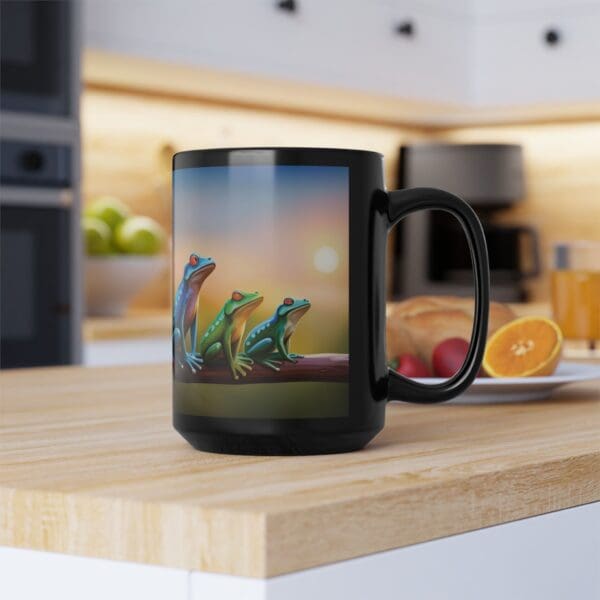 A black *Colorful Frogs Coffee Mug* (available in 11oz and 15oz) featuring an illustration of three frogs on a branch, placed on a wooden kitchen counter. In the background, there are assorted fruits and a bright modern kitchen setup.