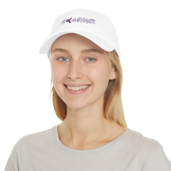 A person wearing the F*ck Cancer Low Profile Baseball Hat, which features white fabric with purple text that reads "F C K CANCER," and a light gray shirt, is smiling at the camera.