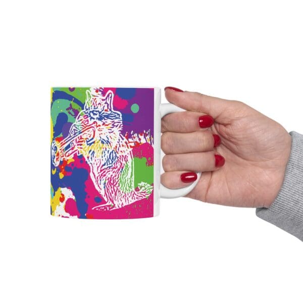 A hand with red-painted nails holds a white Splash Chipmunk Coffee Mug, featuring a colorful, abstract design of a bird playing a trumpet.