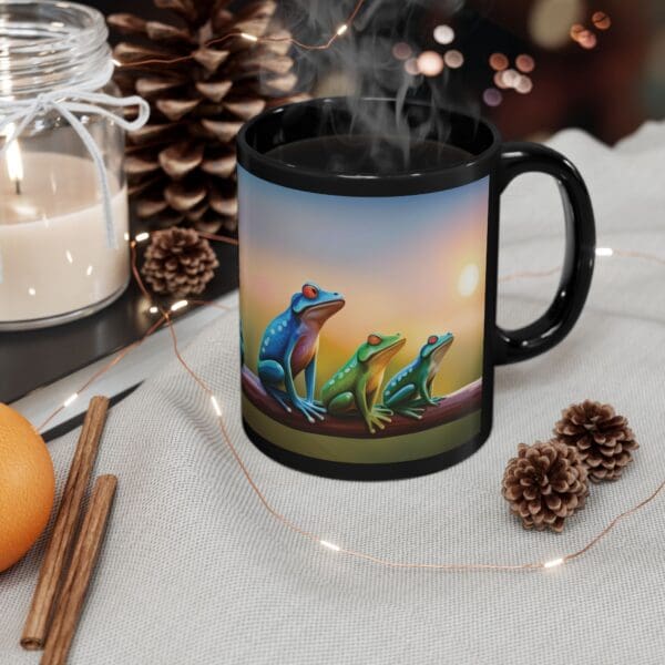 A Colorful Frogs Coffee Mug, available in both 11oz and 15oz sizes, adorned with an image of three vibrant frogs, sits on a table next to a white candle, a pinecone, an orange, cinnamon sticks, and string lights. Steam rises from the mug.