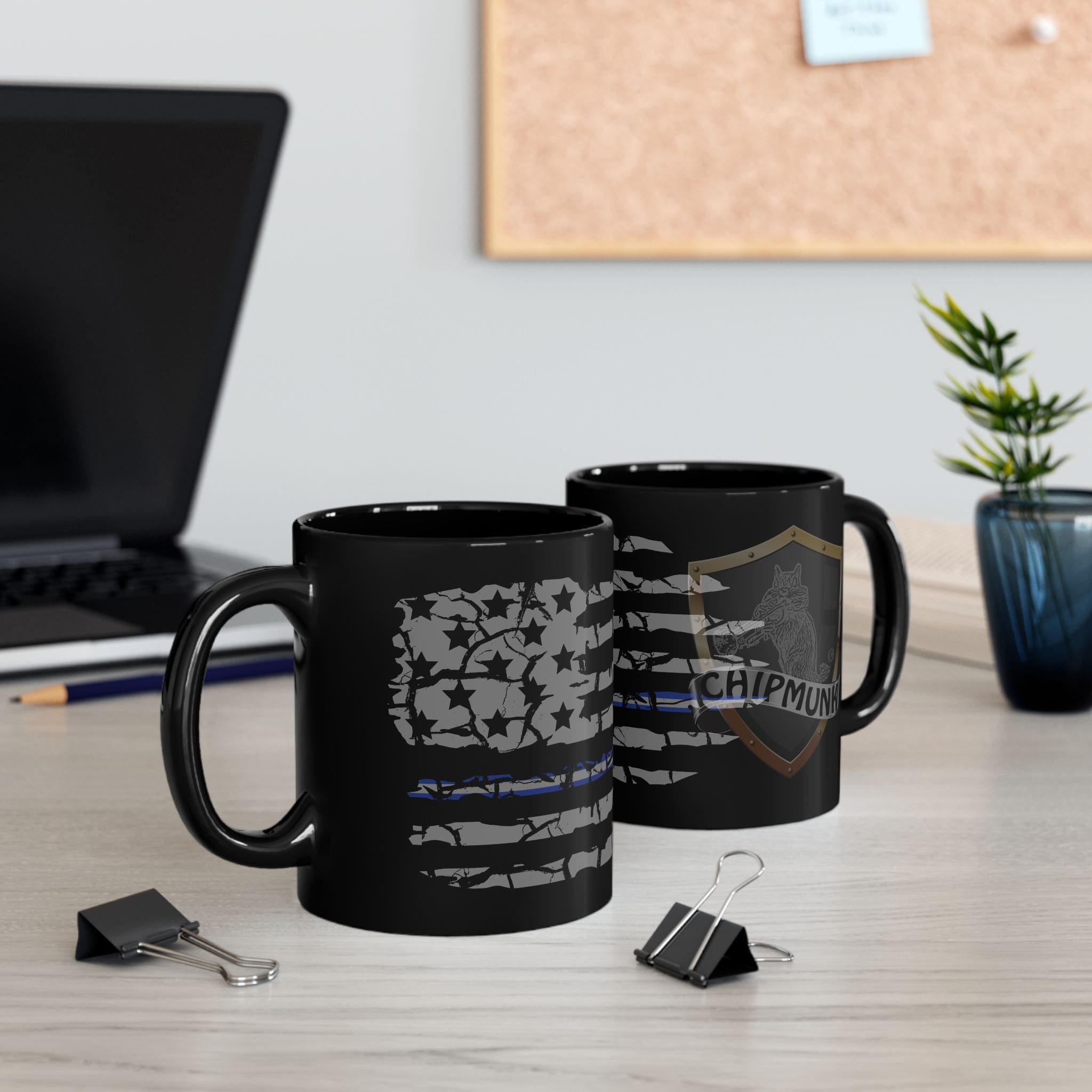 Two EMS Support Coffee Mugs with printed designs on a desk, alongside binder clips, a laptop, and a potted plant. A corkboard is visible in the background.