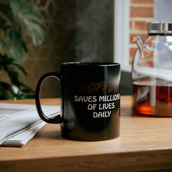 Coffee Saves Lives Coffee Mug placed on a wooden table, with the text "Coffee saves millions of lives daily," accompanied by a glass carafe of coffee and a newspaper in the background.