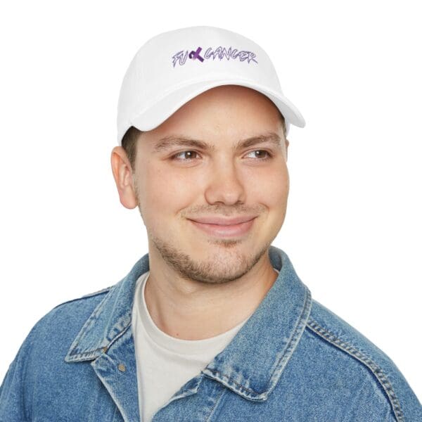 A person smiling and wearing a F*ck Cancer Low Profile Baseball Hat in white with purple text, dressed in a denim jacket over a white shirt.