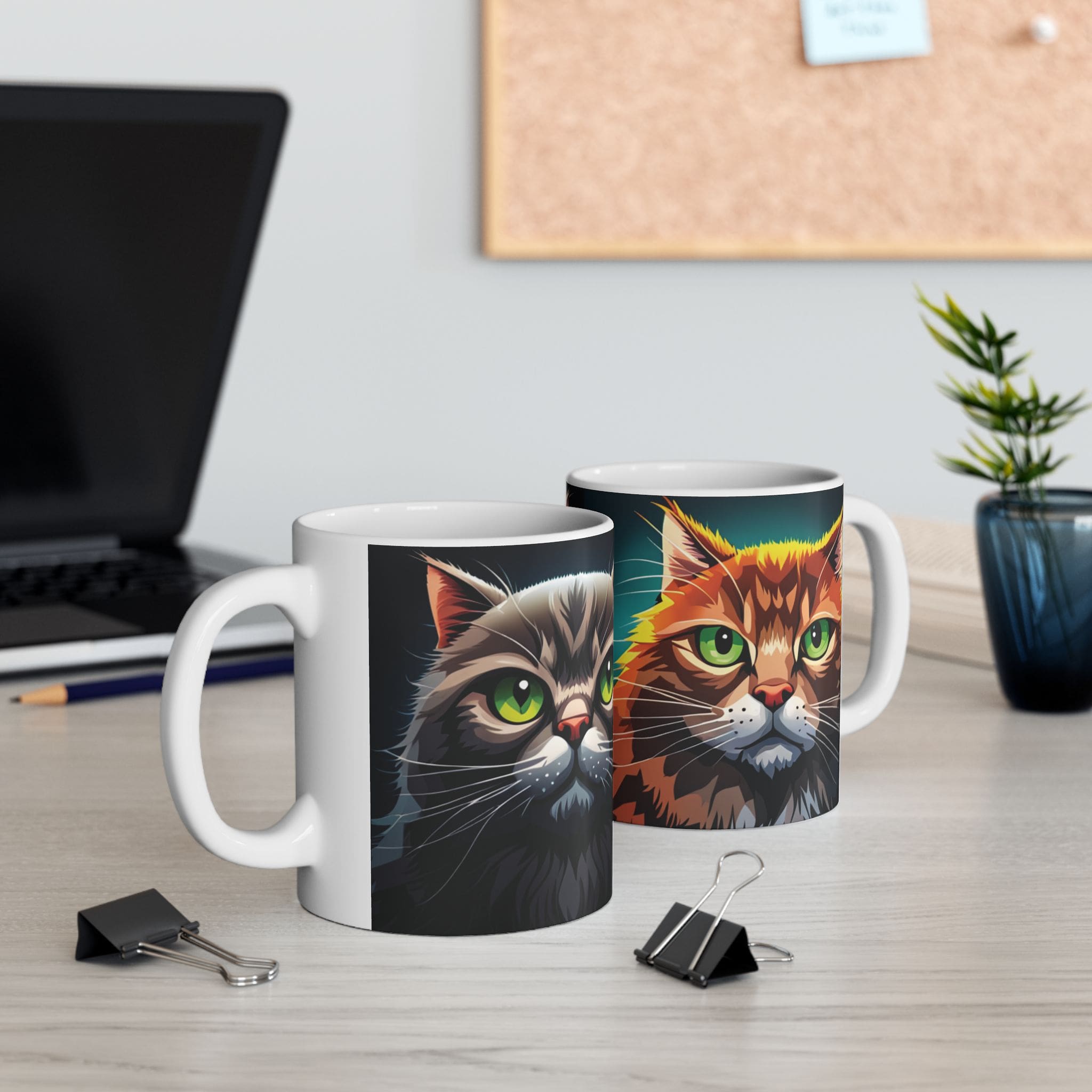 Two Angry Cats Coffee Mugs, each 11oz and featuring illustrated cat faces, sit on a desk near office supplies, a laptop, a small plant, and a corkboard.