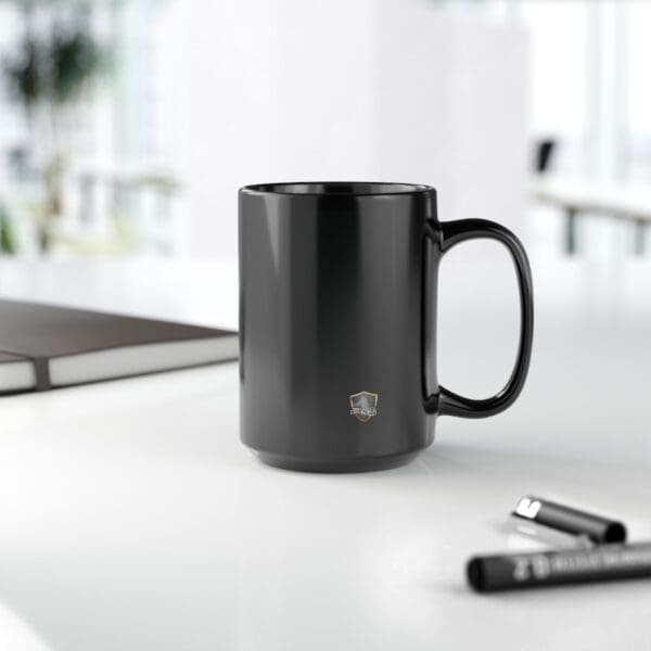 An 11oz Angry Cat Coffee Mug with a small logo is placed on a white office desk alongside pens and a closed laptop.