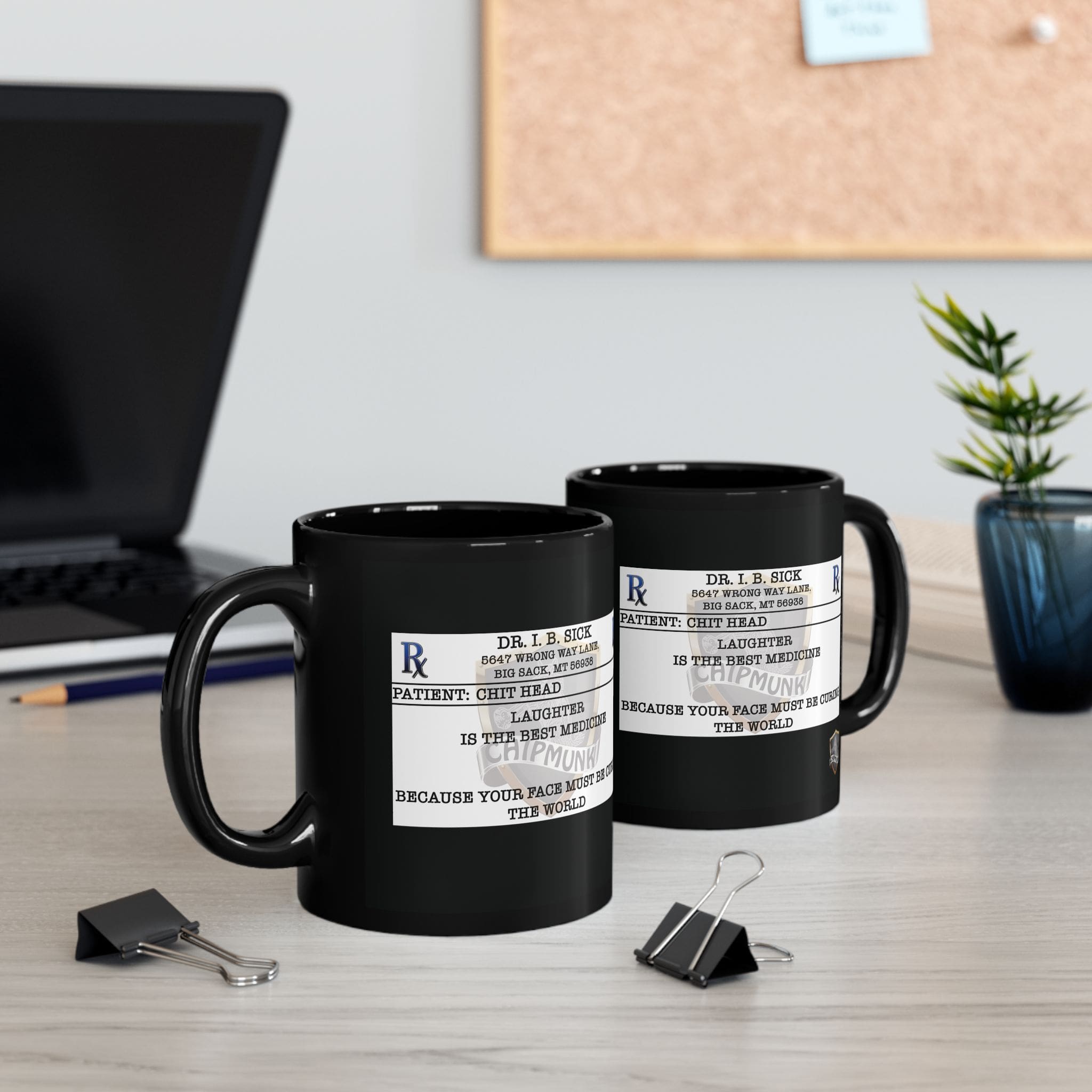 Two "Laughter Is The Best Medicine" coffee mugs with black, humorous prescription label designs sit on a desk alongside a laptop, paper clips, and a small plant.