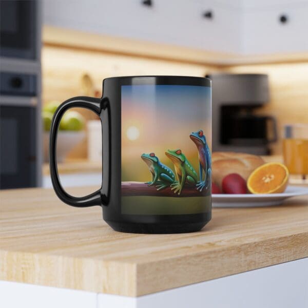 A Colorful Frogs Coffee Mug, available in 11oz and 15oz sizes, featuring an image of three colorful frogs sitting on a branch, is placed on a wooden kitchen counter. In the background, there are fruits, a cutting board, and a coffee machine.