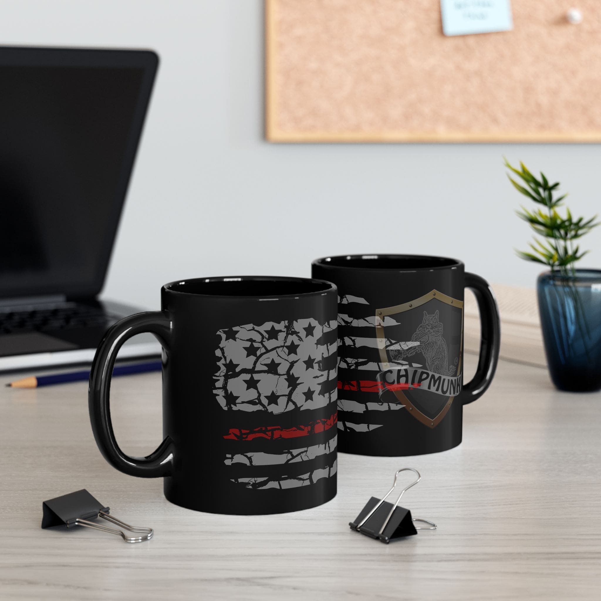 Two Firefighter Support Coffee Mugs with designs on a desk, next to binder clips, a small plant, and partially visible laptop. The background includes a corkboard and a blue sticky note.