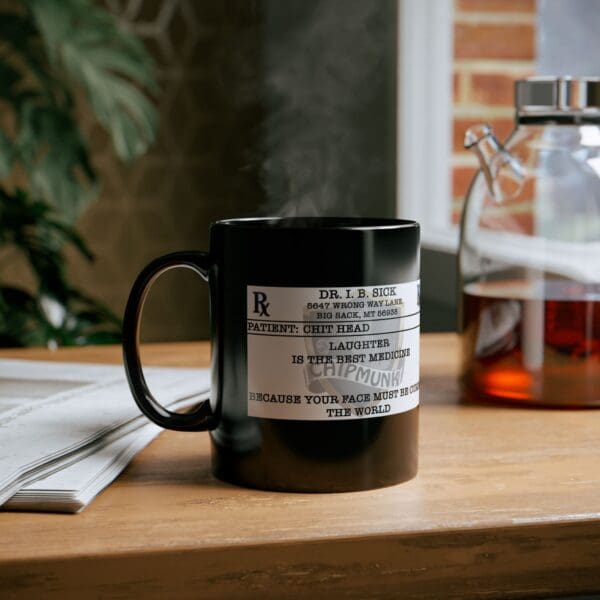 The "Laughter Is The Best Medicine Coffee Mug," adorned with a humorous prescription label that reads, "DR. I.B. SICK - Laughter is the best medicine," sits on a wooden table next to a glass container. Steam rises from the black mug.