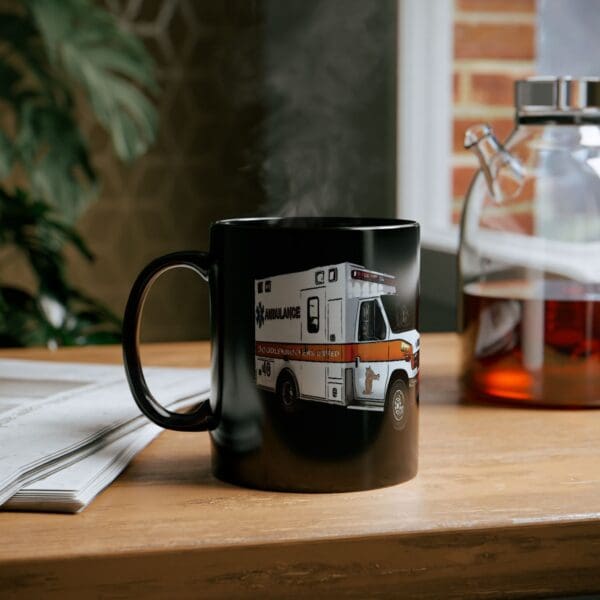 The Ambulance Coffee Mug, which features an image of an ambulance, rests on a wooden table next to a newspaper and a glass coffee pot.