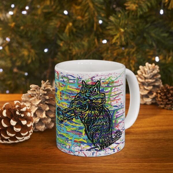 The Cracked Chipmunk Coffee Mug, featuring a vibrant, abstract illustration of a howling wolf, is placed on a wooden table with pinecones and a brightly decorated Christmas tree adorned with lights in the background.