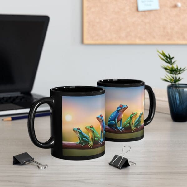 Two Colorful Frogs Coffee Mugs, one 11oz and the other 15oz, sit on a desk next to binder clips, a pen, a small potted plant, and a laptop in the background.