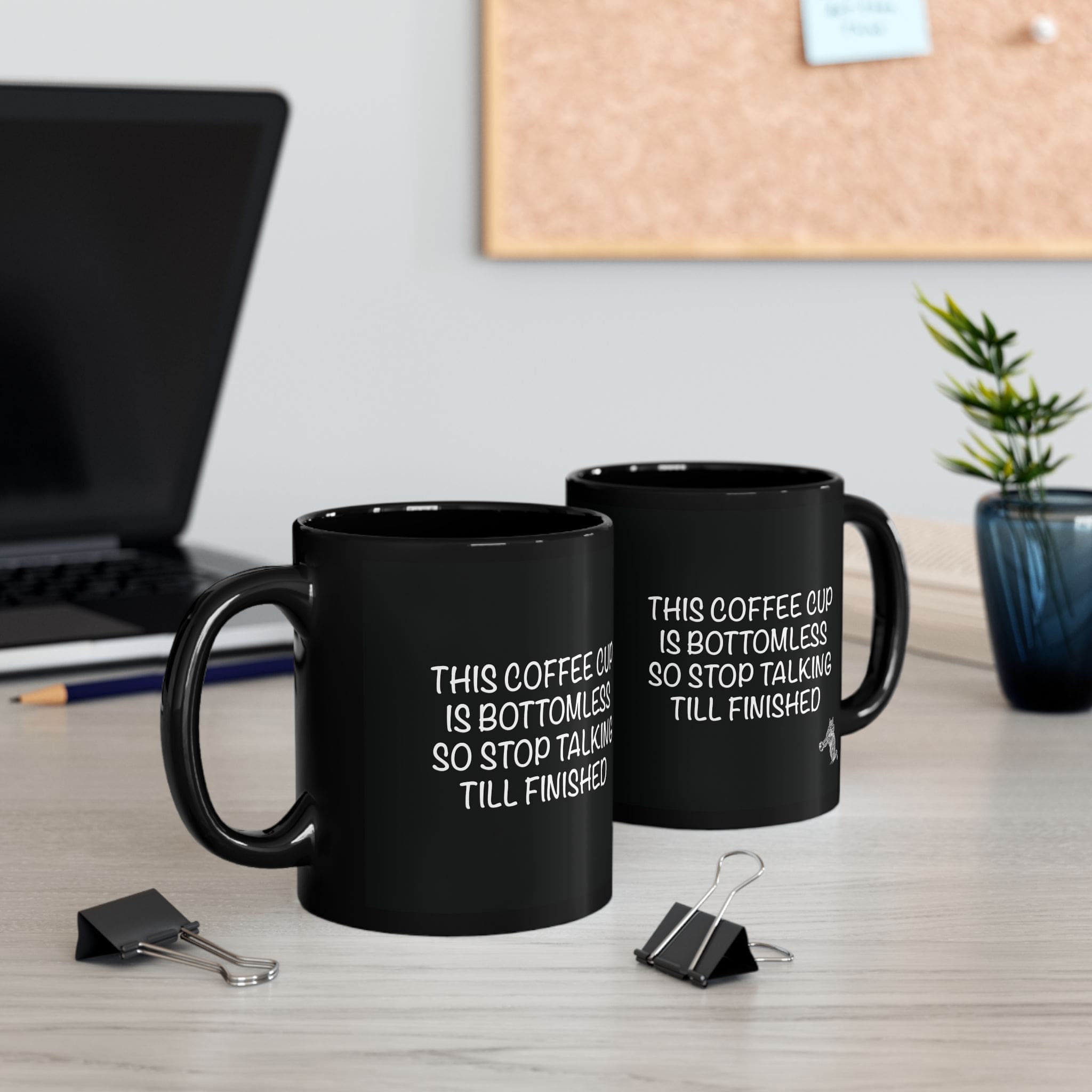 Two Bottomless Coffee Mugs, featuring the text "THIS COFFEE CUP IS BOTTOMLESS SO STOP TALKING TILL FINISHED", sit on a desk near a laptop, small plant, and two black binder clips.