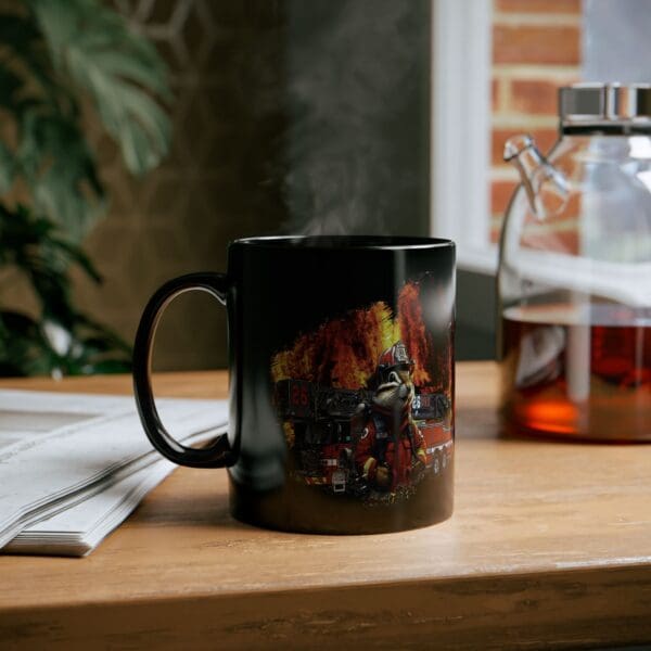 A Firetruck Coffee Cup featuring a graphic of firefighters in action sits on a table next to a glass coffee pot and a newspaper. Steam rises from the mug.