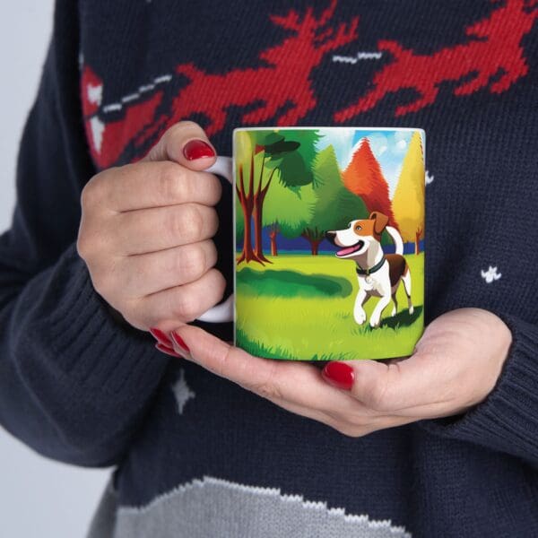 Individual holding a Playful Dog Coffee Mug 11oz featuring a colorful illustration of a dog in a park. The person is wearing a dark sweater with a red and white reindeer design.