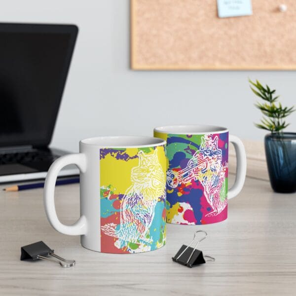 Two Splash Chipmunk Coffee Mugs with colorful animal designs stand on a desk next to black binder clips. A laptop, a small plant, and a corkboard are in the background.