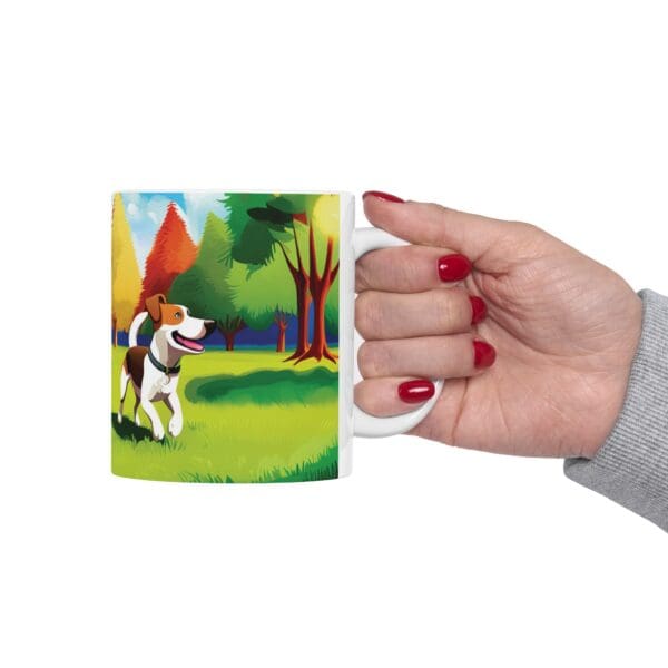 A hand with red-painted nails holds a Playful Dog Coffee Mug 11oz, featuring an illustration of a dog in a colorful outdoor park scene.