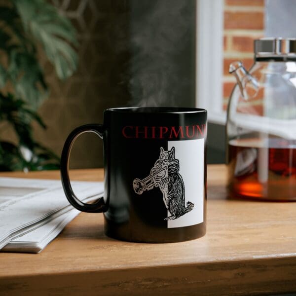 The Chipmunk Coffee Mug, featuring a cartoon boar and the text "CHIPMUNK," sits on a table next to a newspaper and a glass container. Steam rises from the black coffee mug, with a plant and window visible in the background.