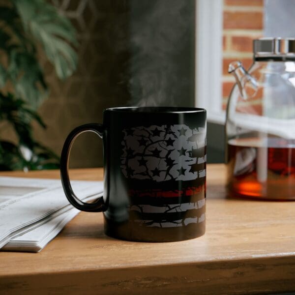 A Firefighter Support Coffee Mug with an American flag design sits on a wooden table next to a folded newspaper and a glass jar of coffee. Steam rises from the mug.