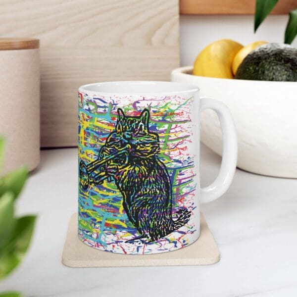 Cracked Chipmunk Coffee Mug featuring a colorful illustration of a raccoon playing a trumpet, placed on a beige coaster. The background includes a bowl of fruits and leafy greens on a countertop.