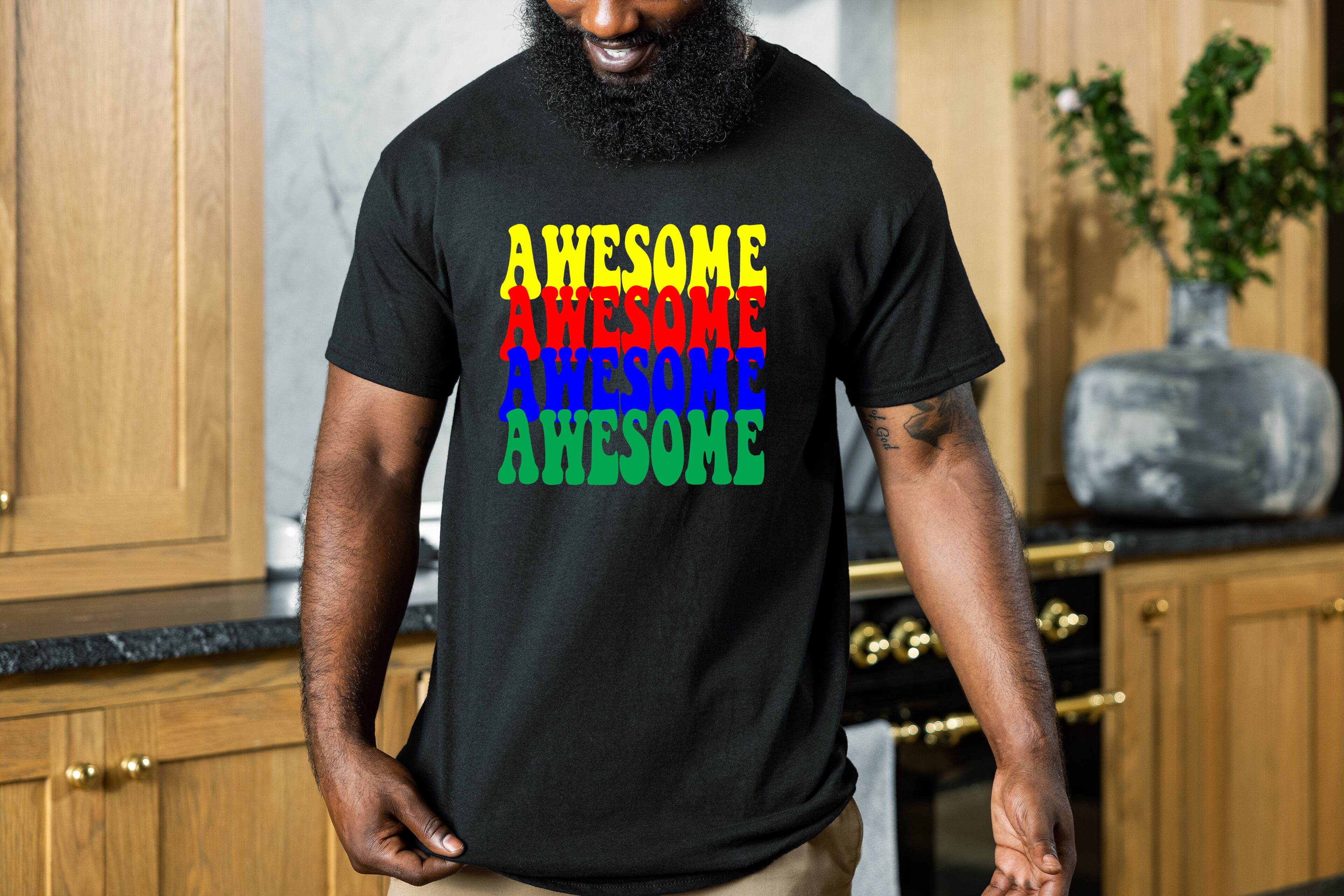 A person wearing the Awesome Shirt, a black t-shirt with the word "Awesome" printed multiple times in different colors, stands in a kitchen with wooden cabinets and a black countertop.