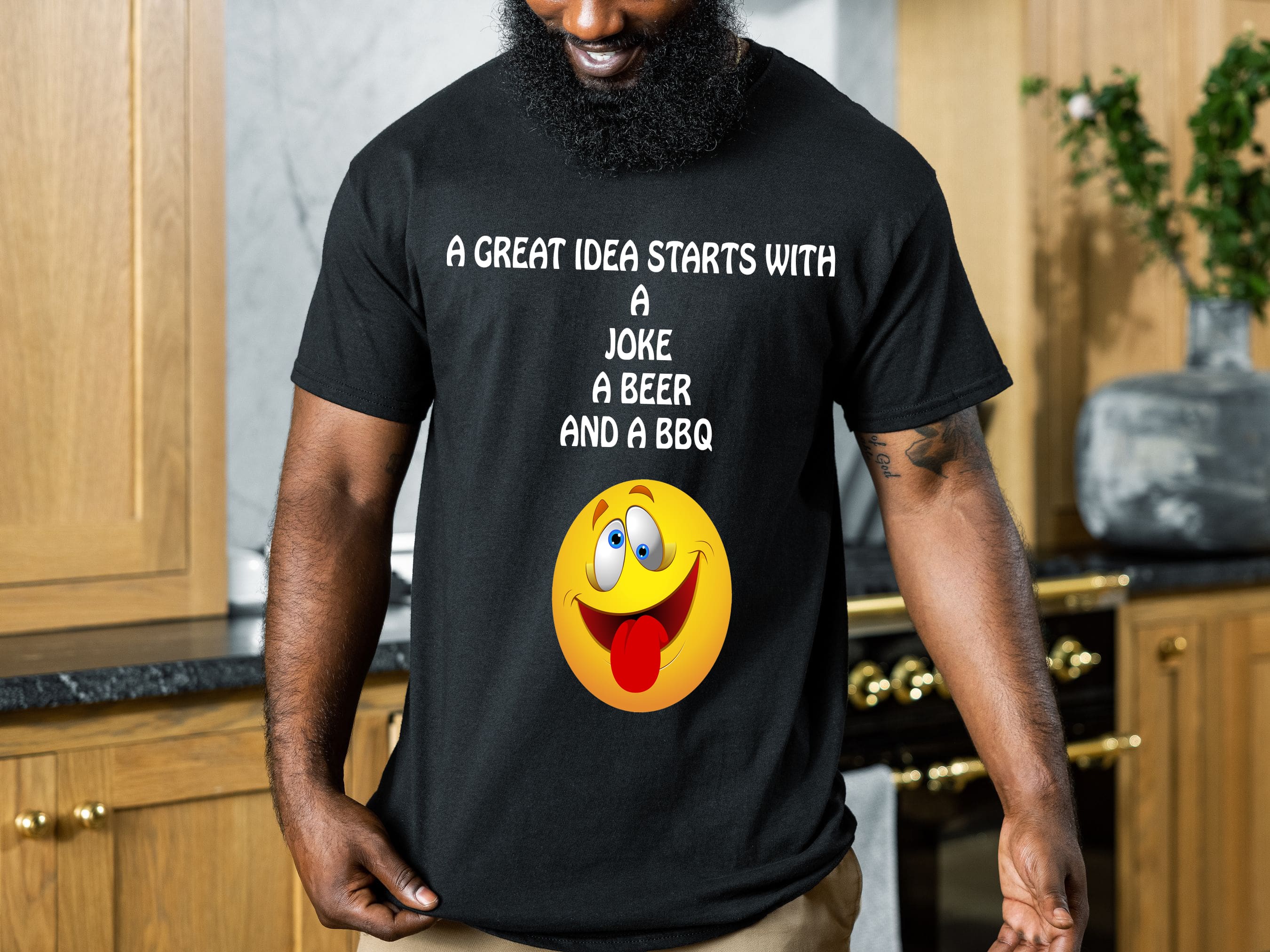 A person wearing the Great Idea T-Shirt, which is black and features the text "A GREAT IDEA STARTS WITH A JOKE, A BEER, AND A BBQ" above a smiling emoji face.