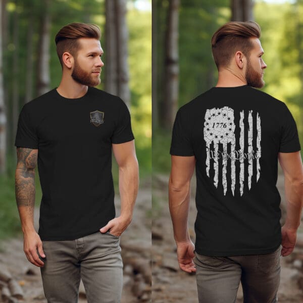 A man stands in a wooded area, wearing an American Pride T-Shirt with a small emblem on the front and a large design on the back featuring the year "1776" and an abstract flag.