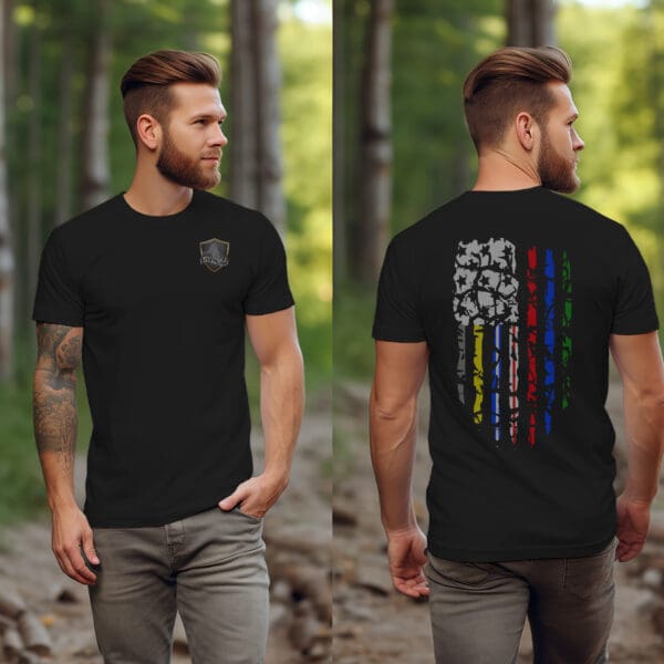 A man in a wooded area is depicted from the front and back, wearing the Distressed American Flag Shirt with Military & First Responder Support Colors. The black T-shirt features a small emblem on the chest and a distressed multicolored flag design on the back. He sports a beard and has tattoos.