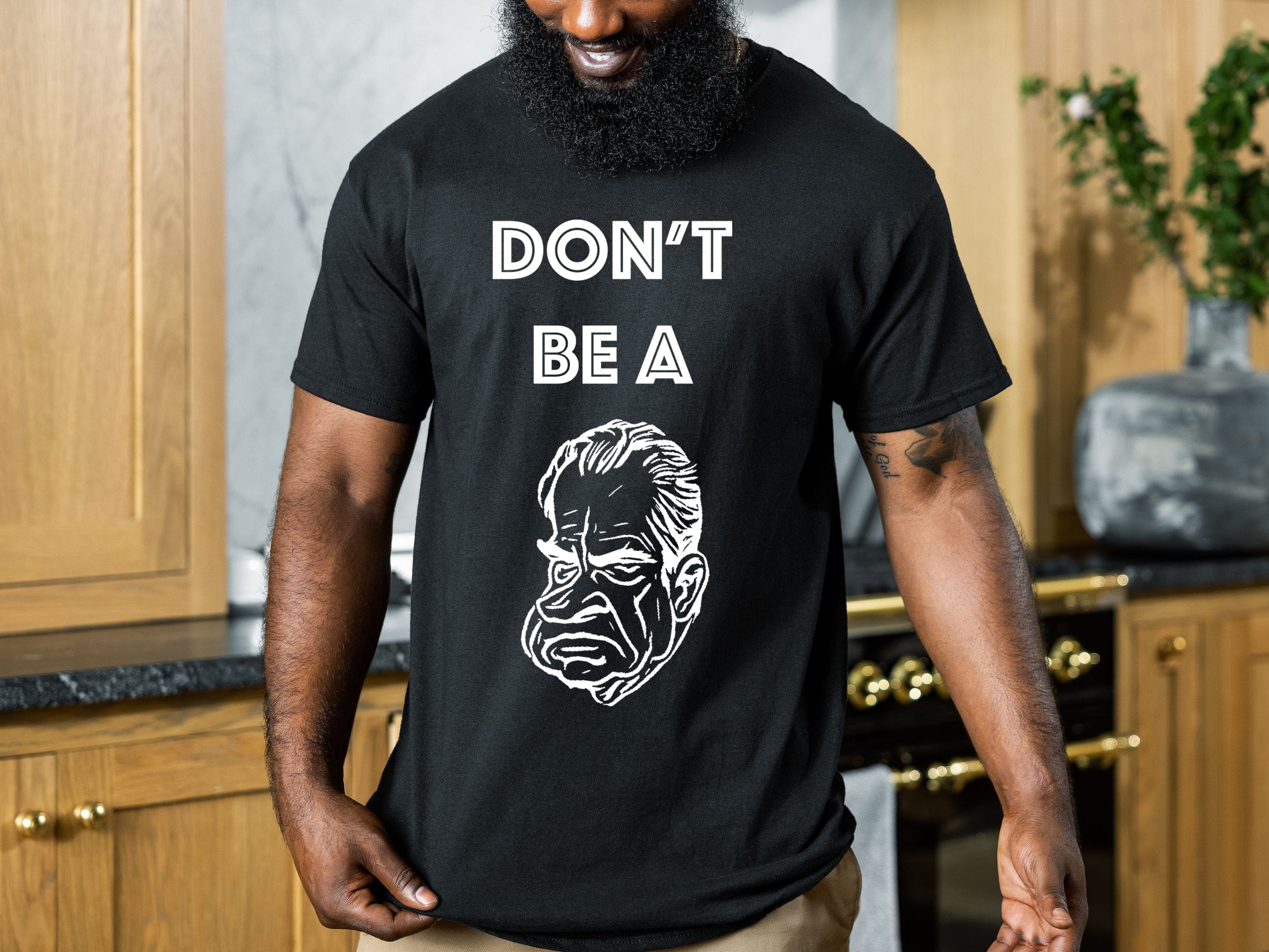 A person wearing a "Don't Be A... Tee" with the text "DON'T BE A" above an illustration of Richard Nixon's face, standing in a kitchen with wooden cabinets and a plant in the background.