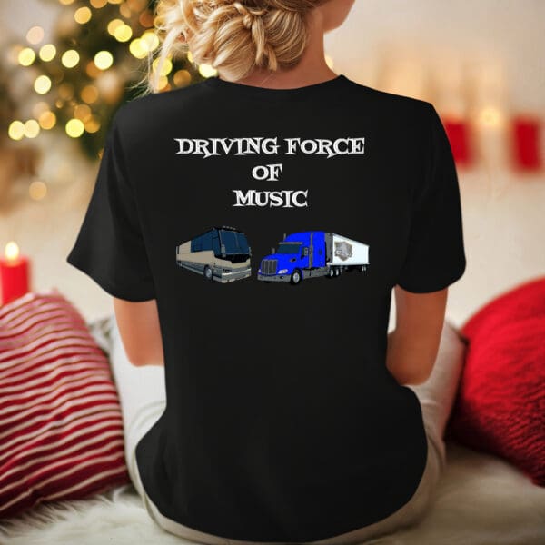 A person wearing the Driving Force T-Shirt, featuring graphics of a tour bus and a truck along with the text "DRIVING FORCE OF MUSIC," stands in front of a background adorned with a Christmas tree and festive decorations.