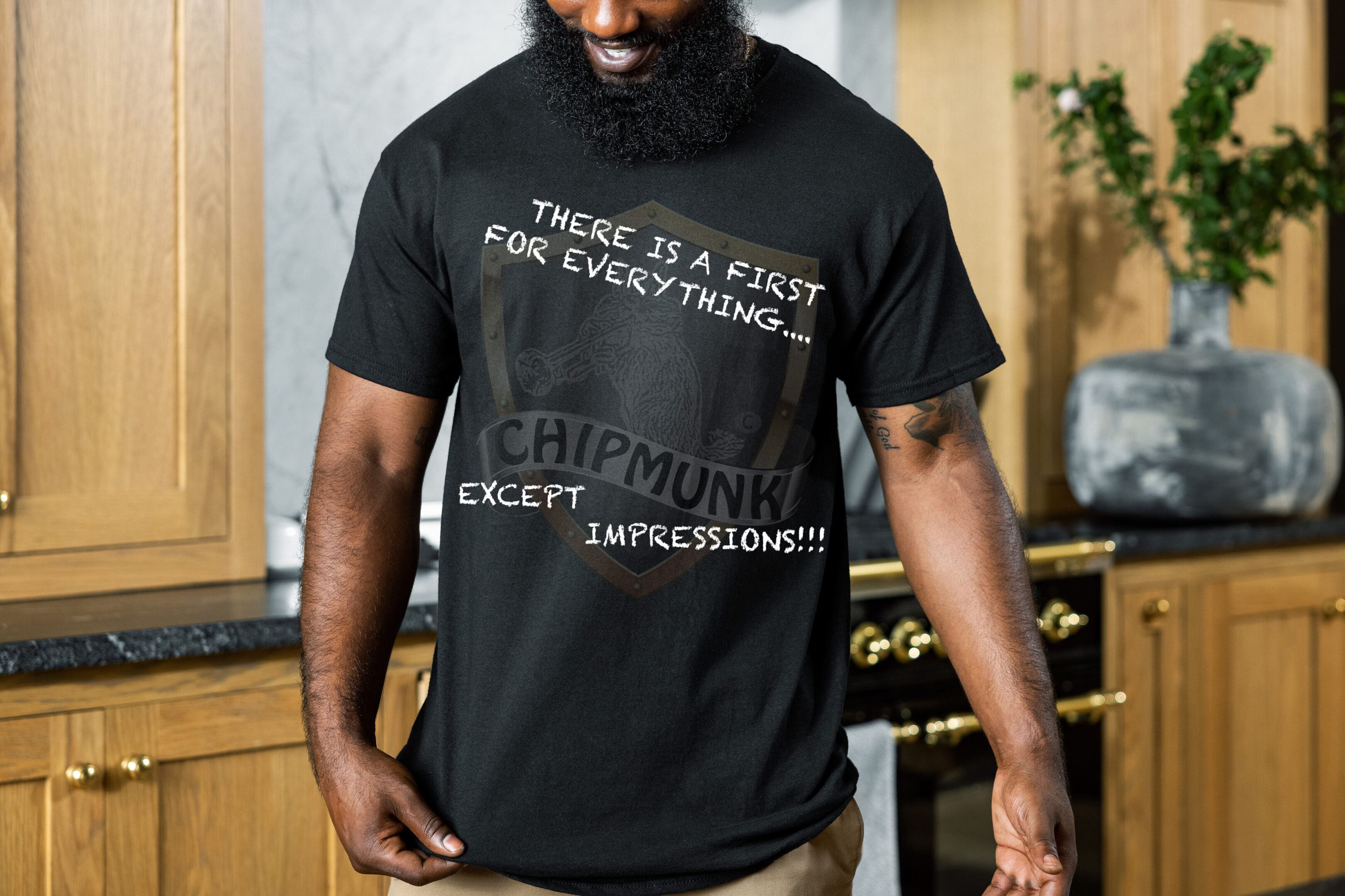 A person wearing a "There's a First for Everything... Except Impressions!" T-Shirt stands in a kitchen with wooden cabinetry and black countertops.