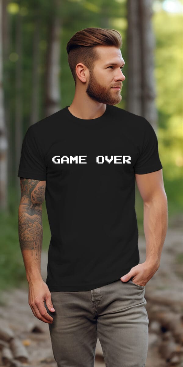 A bearded, tattooed man stands outdoors on a wooded path, wearing a black Game Over T-Shirt.