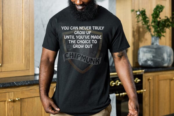 A person wearing a "You Can Never Truly Grow Up" T-shirt featuring the text "You can never truly grow up until you've made the choice to grow out. Chipmunk!" stands in a kitchen setting.