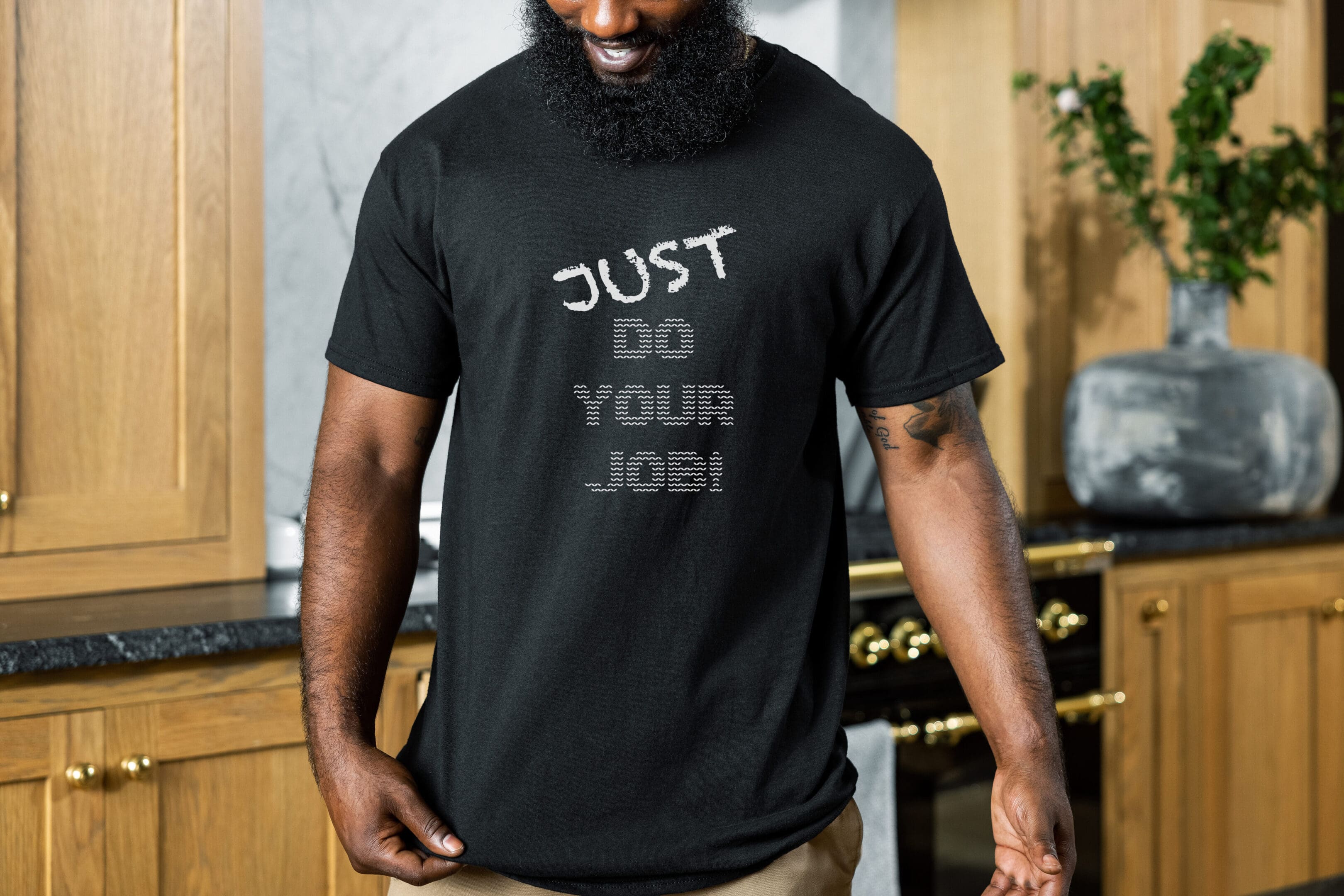 A person with a beard wearing the "Just Do Your Job!" T-Shirt, standing in a kitchen.