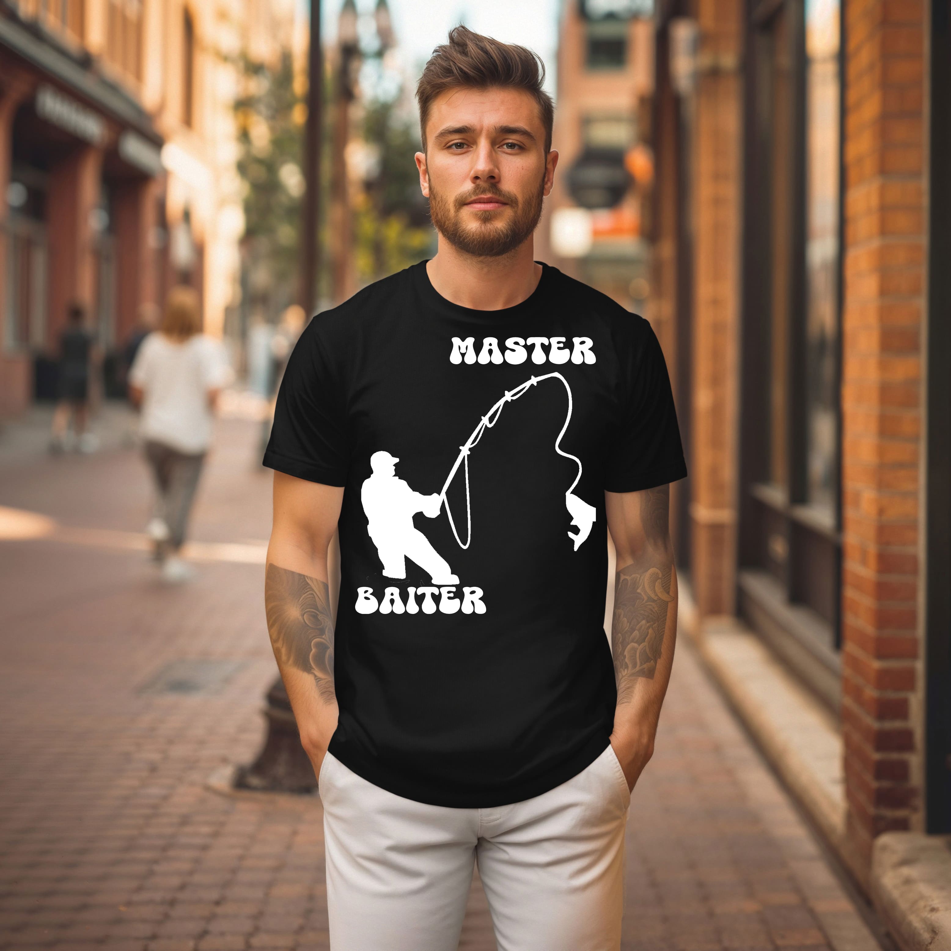 A man wearing the "Master Baiter" black shirt, featuring a fishing graphic and the product name printed on it, stands on a brick street with shops and a pedestrian in the background.