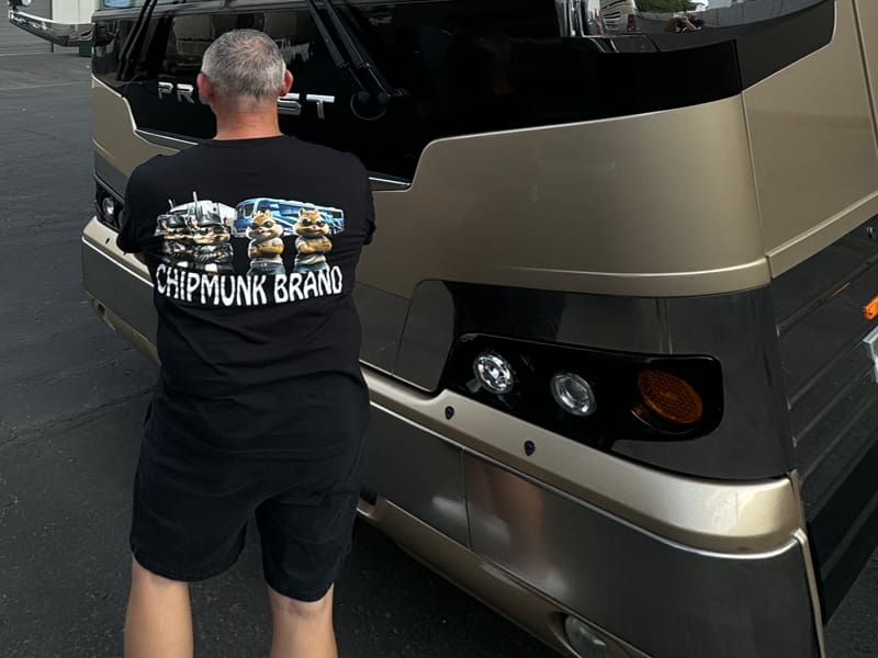 A person wearing a "Chipmunk Brand" T-shirt stands with their back to the camera, facing a large vehicle.