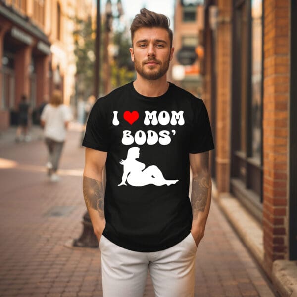 A man standing on a city street wearing an "I ❤️ Mom Bods T-Shirt" that features an illustration of a woman.