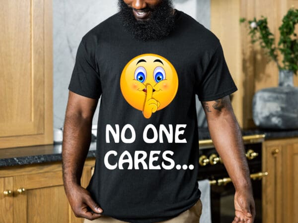 A man wearing the "No One Cares" T-shirt, which features a black design with a "shushing" emoji and the text "NO ONE CARES...", is standing in a kitchen.