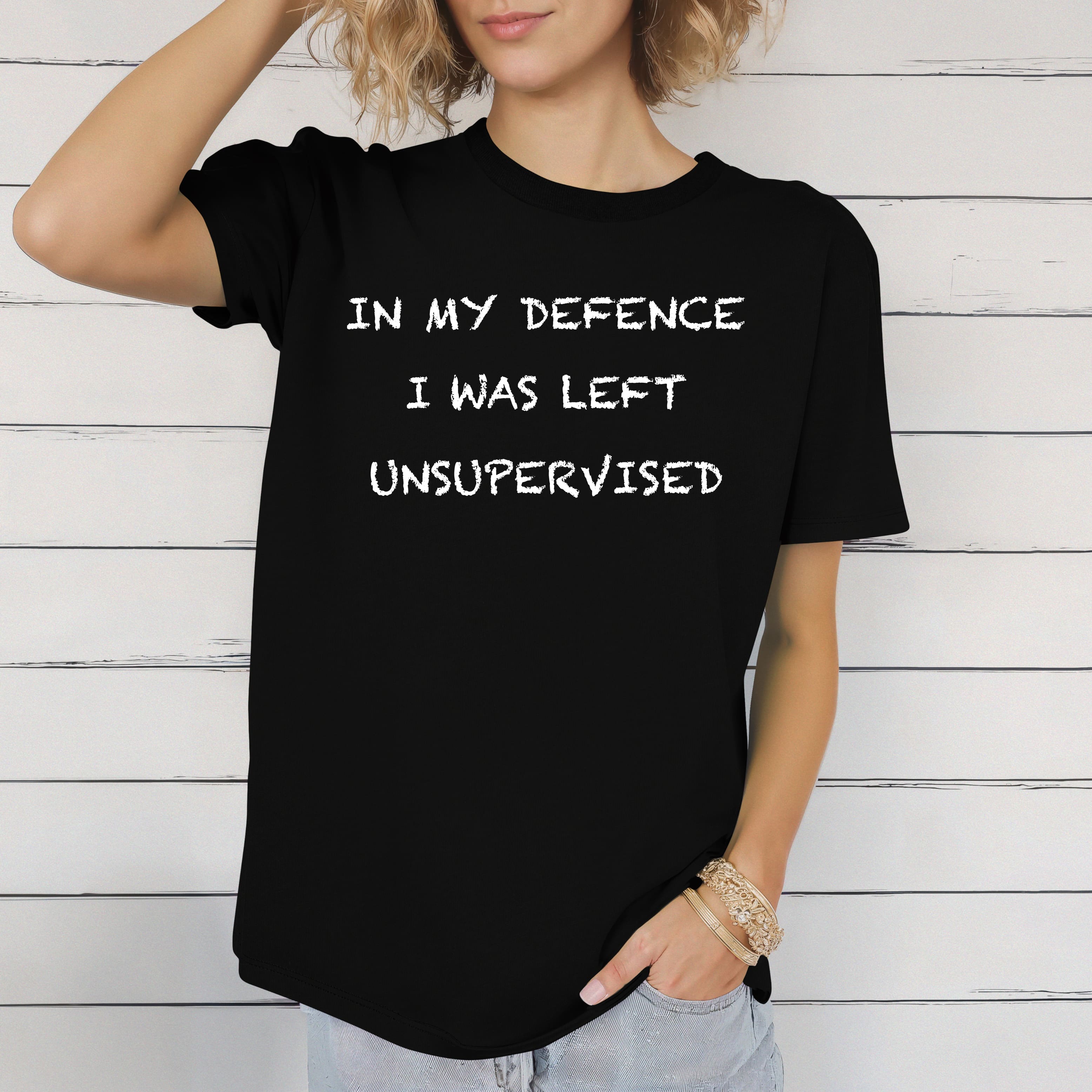 Person wearing the "Unsupervised Mischief T-Shirt," standing against a white wooden wall.