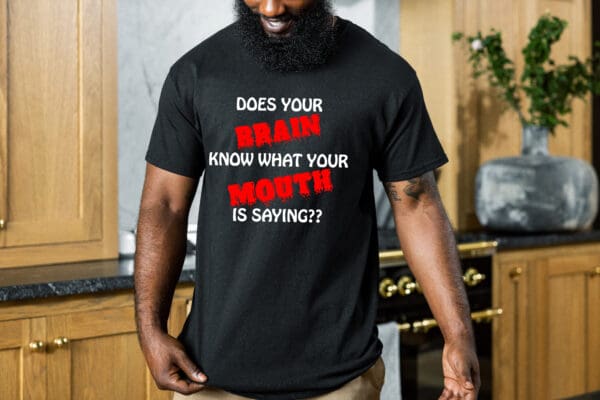 A person with a beard wearing the "Your Brain T-Shirt" with the text: "DOES YOUR BRAIN KNOW WHAT YOUR MOUTH IS SAYING??" standing in a kitchen.