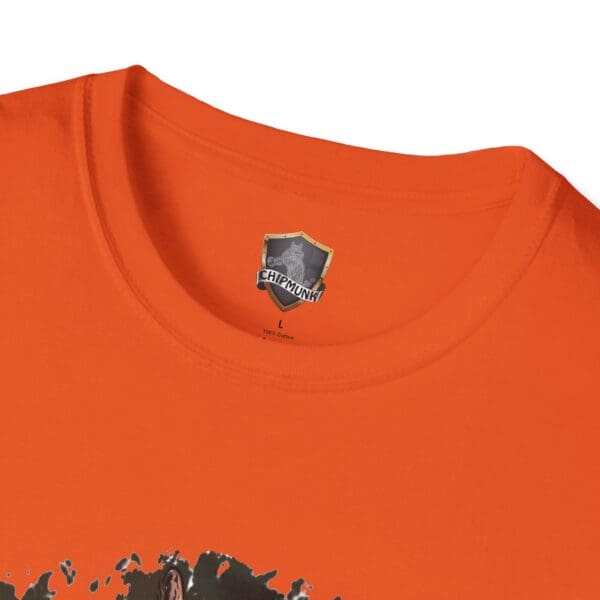 A close-up of an OG Chipmunk T-Shirt in orange, featuring a label with a shield design and the word "Chipmunk," along with a partially visible graphic at the bottom.