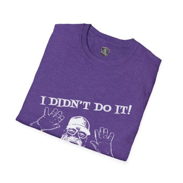 A folded purple T-shirt featuring the iconic design of George the Roadie, showing a person raising their hands, adorned with the text "I Didn't Do It! I Was Framed!!!