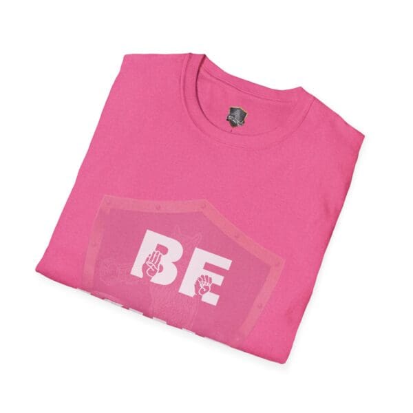 A folded pink t-shirt titled "Be Kind in Sign Language" with "BE" printed in white letters, adorned with two small raised fist graphics.